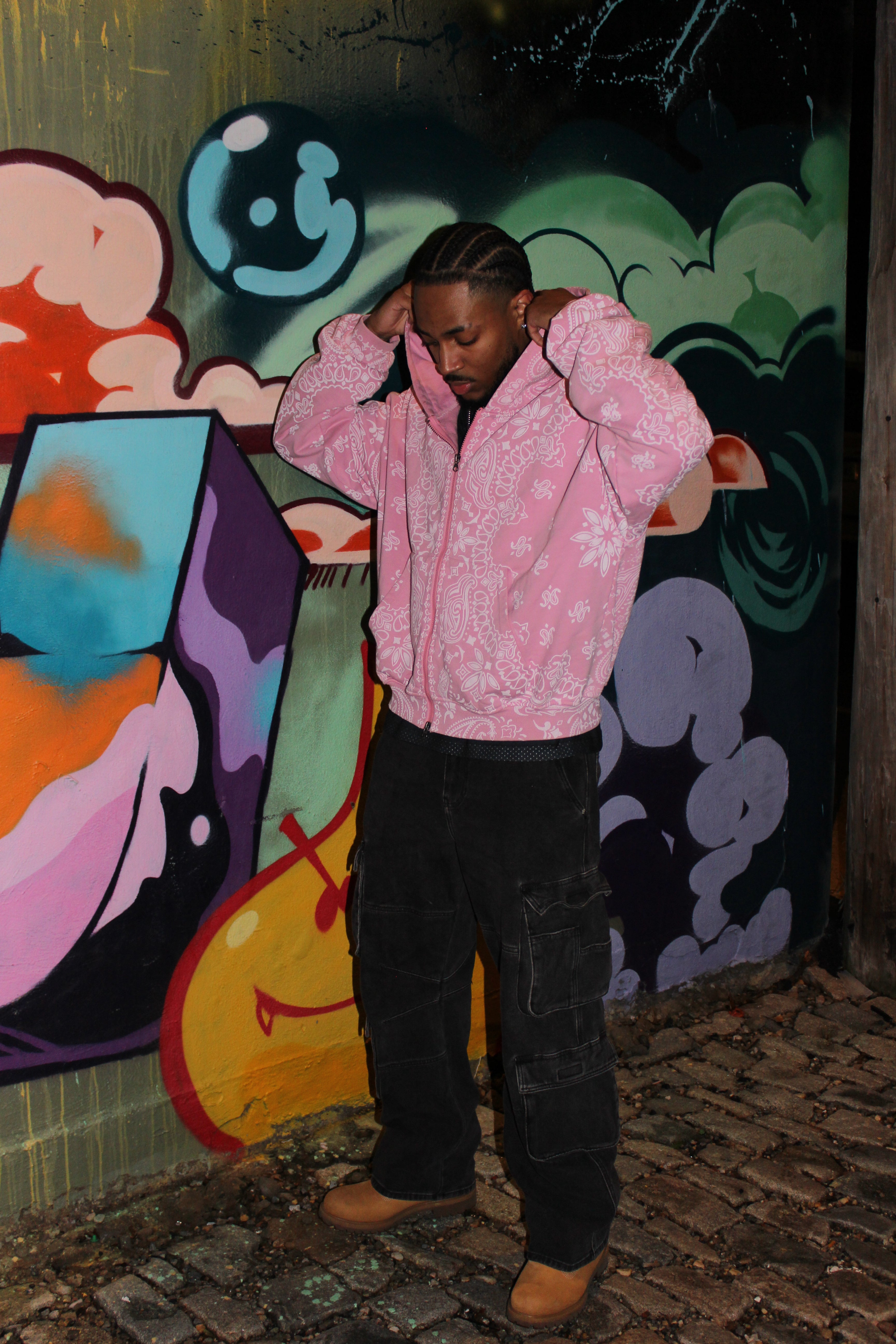 Person wearing a pink hoodie standing in front of colorful graffiti art.