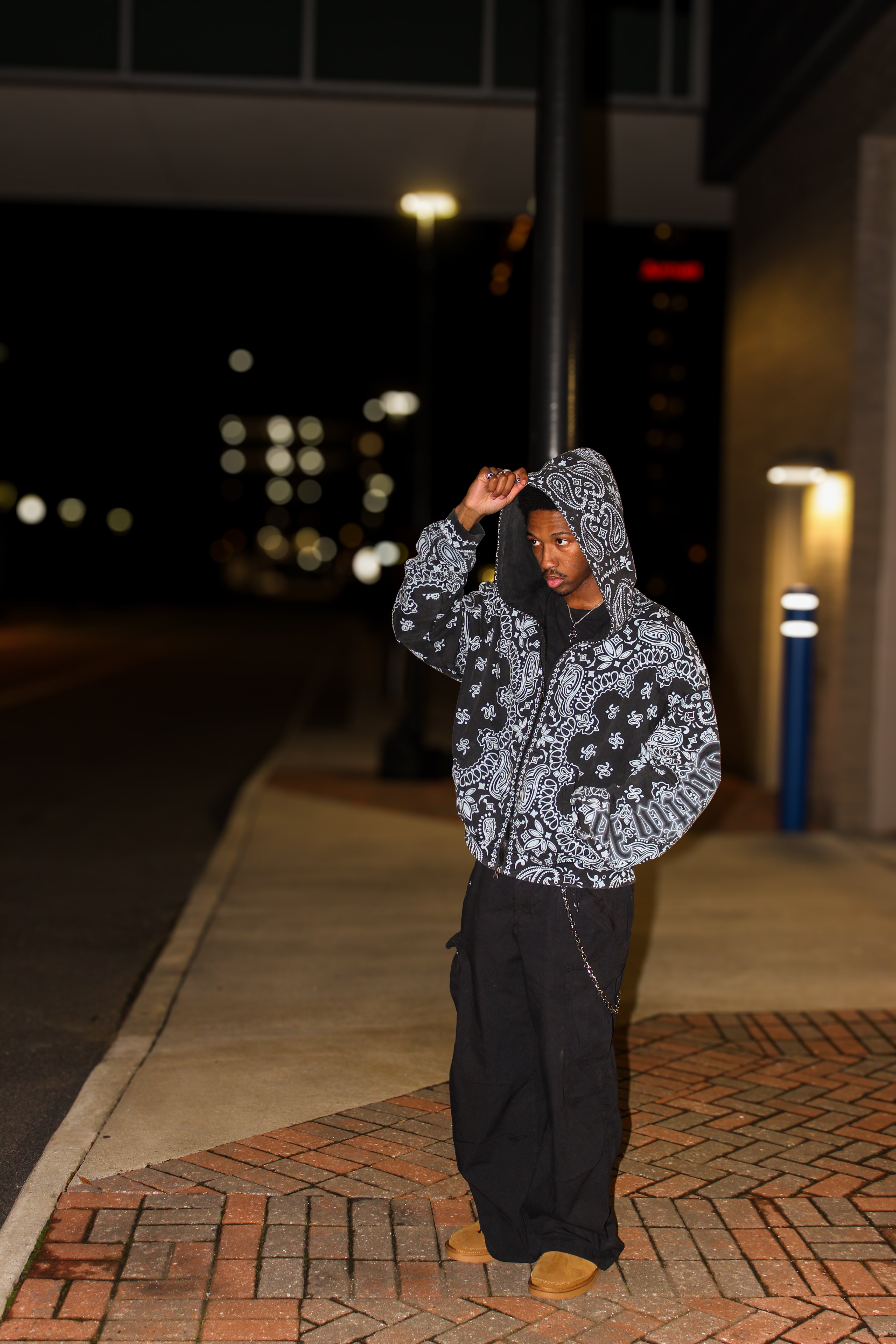Person wearing a black paisley-patterned CuttinUp Jacket standing on a sidewalk at night.
