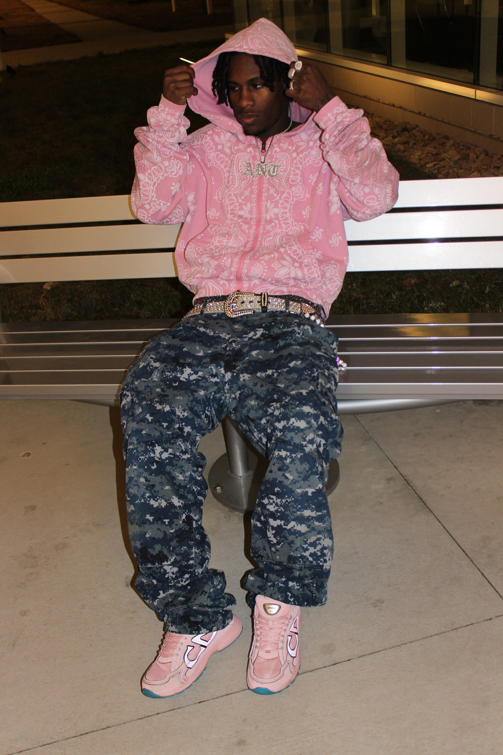 Person wearing a pink CuttinUp Jacket and camouflage pants sitting on a bench.