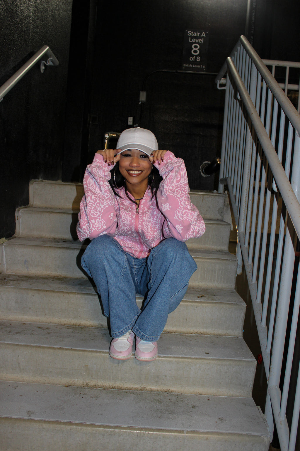 Person sitting on stairs wearing a pink CuttinUp jacket and blue jeans.
